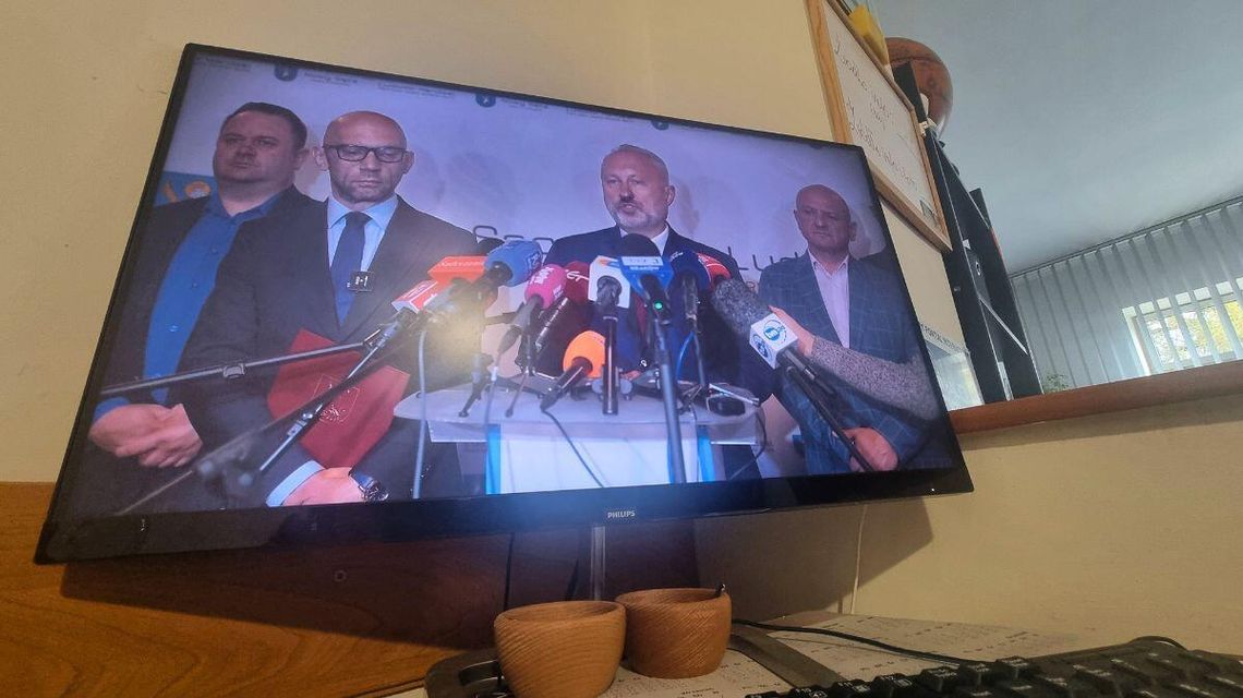 zdjęcie przedstawia kilku mężczyzn przed mikrofonami postawionymi na pulpicie