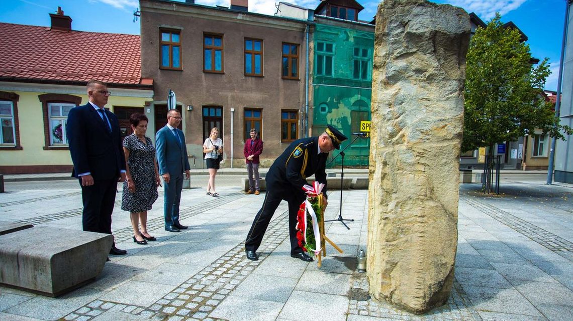 mężczyzna składa wieniec przed obeliskiem, za nim stoją jedna kobieta i dwóch mężczyzn z garniturach