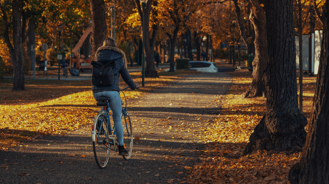 zdjęcie przedstawia kobietę na rowerze, która jedzie przez park