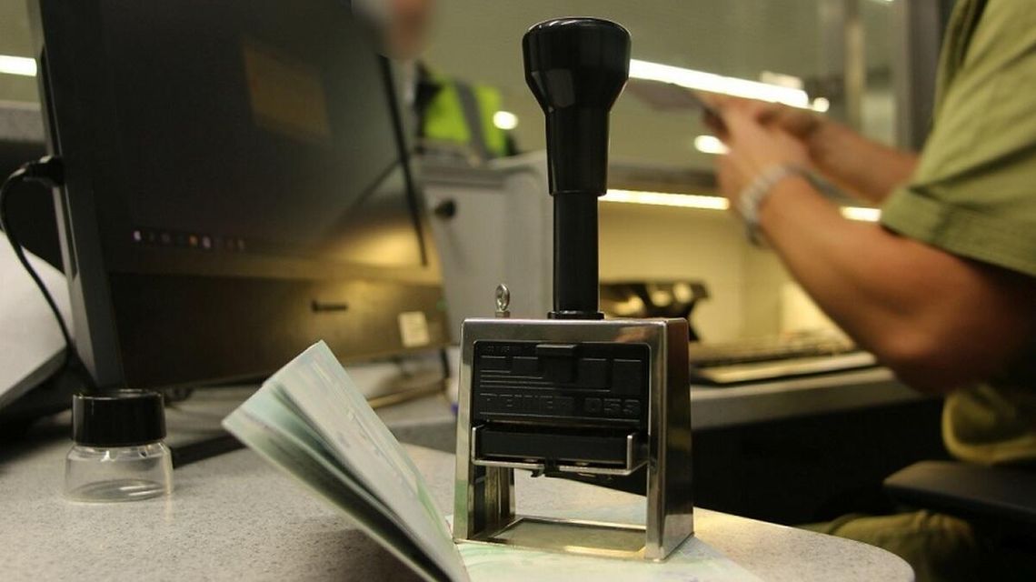 zdjęcie przedstawia pieczątkę na biurku w tle paszport i mężczyzna w mundurze