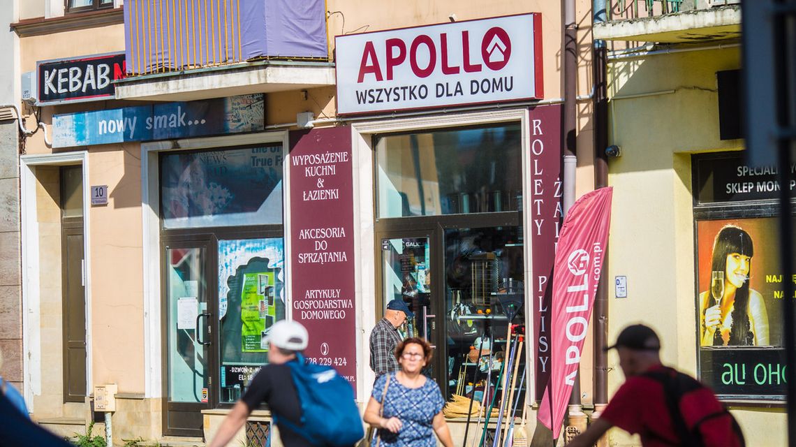 Sklepy Apollo „Wszystko dla domu” ruszają z akcją wietrzenia magazynów. Rabaty dla klientów ludzie przechodzący chodnikiem przed sklepem w gorlicach, w tle witryny sklepu Apollo w Gorlicach