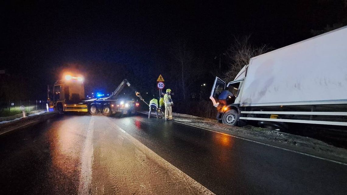 samochód ciężarowy w rowie, przed nim strażacy i samochód holowniczy