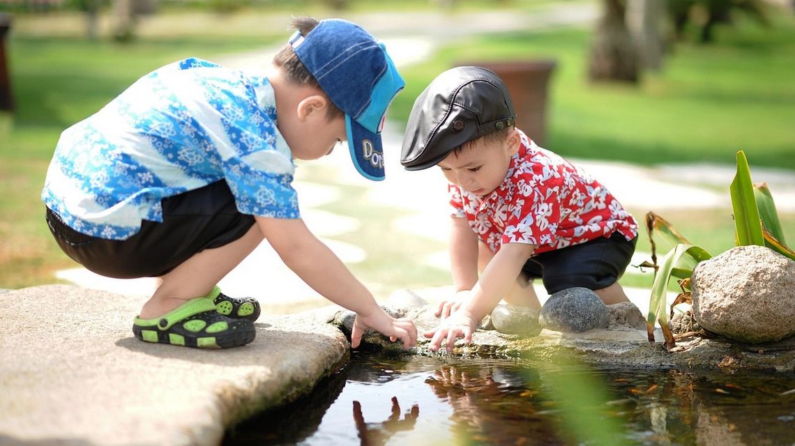 zdjęcie przedstawia dwóch małych chłopców bawiących się nad wodą