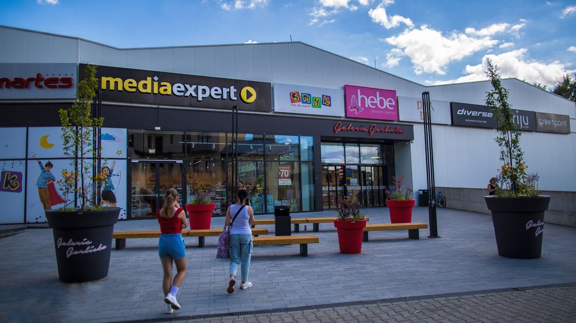 zdjęcie przedstawia wejście do galerii gorlickiej, przed którą stoją ławeczki i donice z roślinami