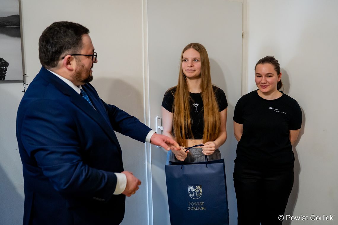 zdjęcie przedstawia dwie kobiety i mężczyznę, który wręcza im prezent