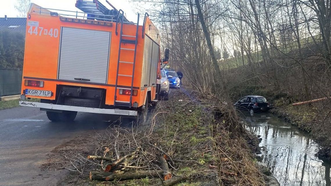 zdjęcie przedstawia samochód w potoku, obok straż pożarna
