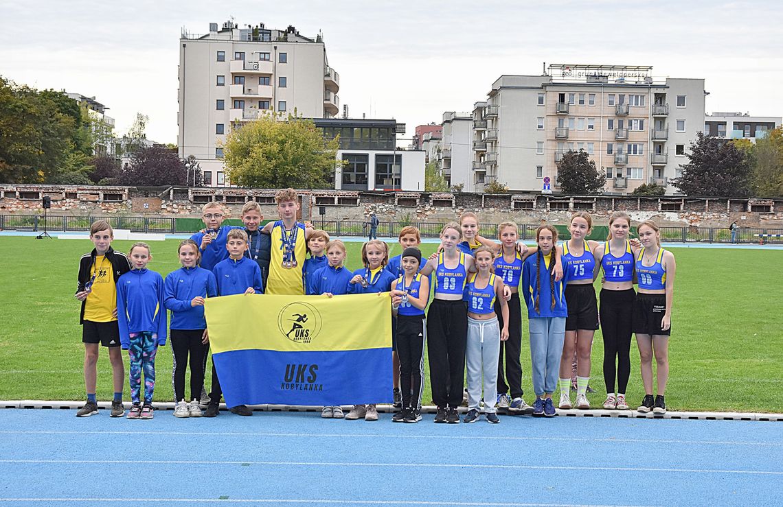 grupa dziewcząt i chłopców w strojach sportowych na stadionie lekkoatletycznym w Krakowie