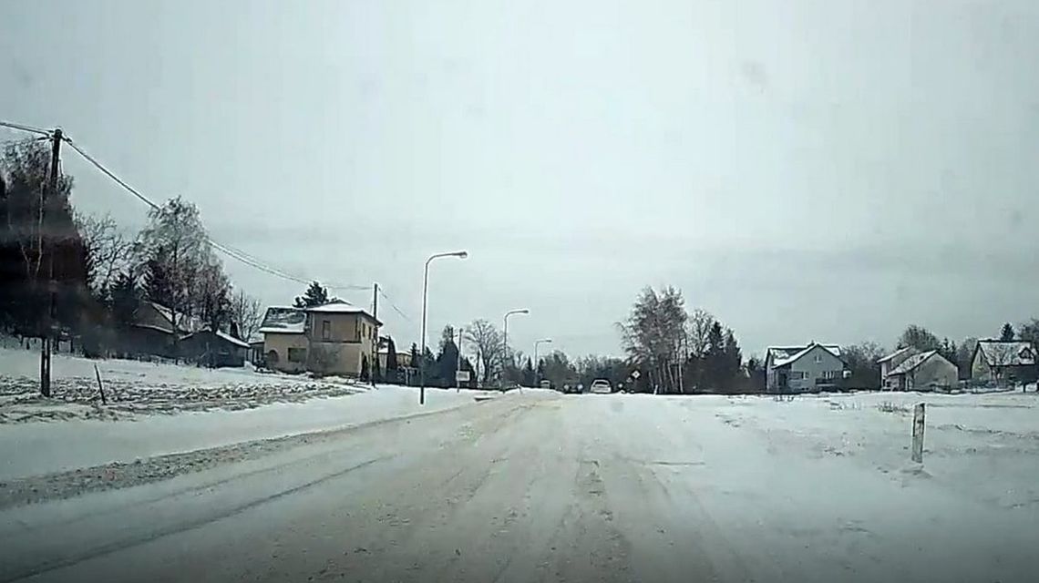 zdjęcie przedstawia śnieg zalegający na jezdni i polach, w tle zabudowania