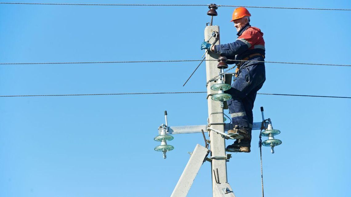 zdjęcie przedstawia mężczyznę na słupie energetycznym w kasku