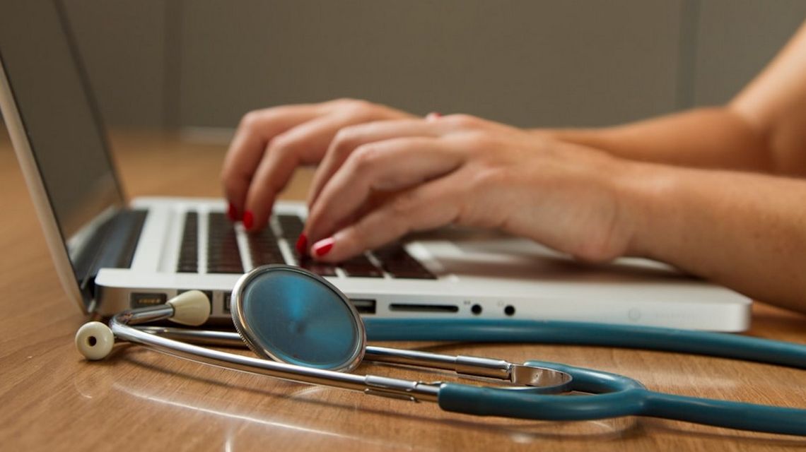 Teleporada — czym jest i jak się do niej przygotować? zdjęcie przedstawia ręce kobiety na klawiaturze laptopa, obok stetoskop lekarski