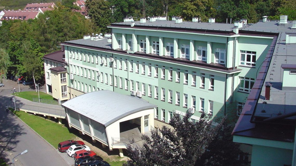 zdjęcie przedstawia duży budynek szpitala w Jaśle o zielonej elewacji, przed którym stoją samochody