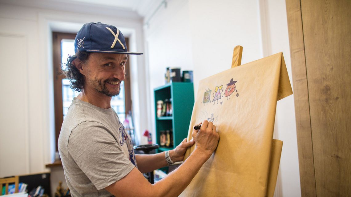 mężczyzna w czapeczce rysujący na tablicy komiks w gorlickim cenrtum kultury