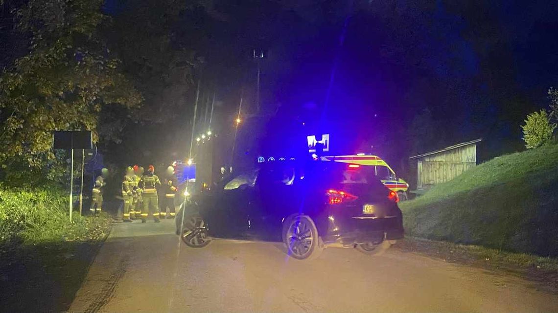 zdjęcie przedstawia samochód na drodze, obok strażacy, zdjęcie wykonane w nocy