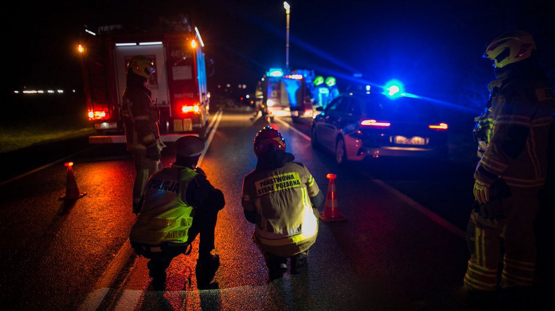 zdjęcie przedstawia policjanta i strażaka kucającego na jezdni