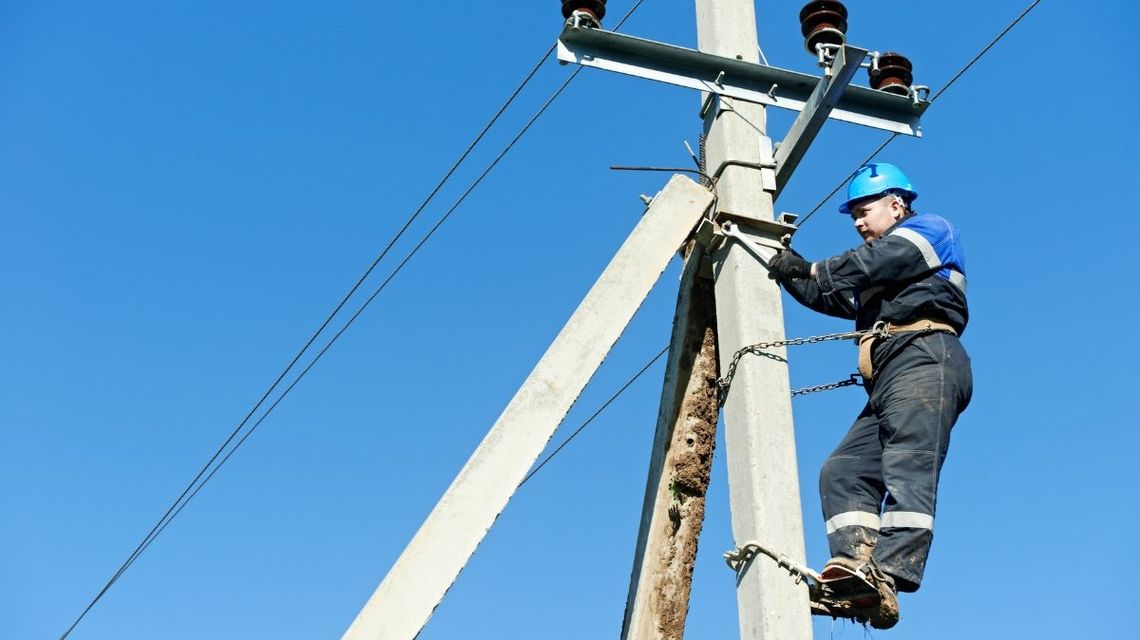 mężczyzna przyczepiony do słupa energetycznego łańcuchami, instaluje obejmę