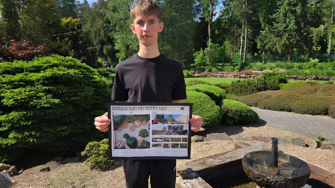 zdjęcie przedstawia portret młodego chłopaka, który trzyma przed sobą planszę, za nim jest ogród z zielenią