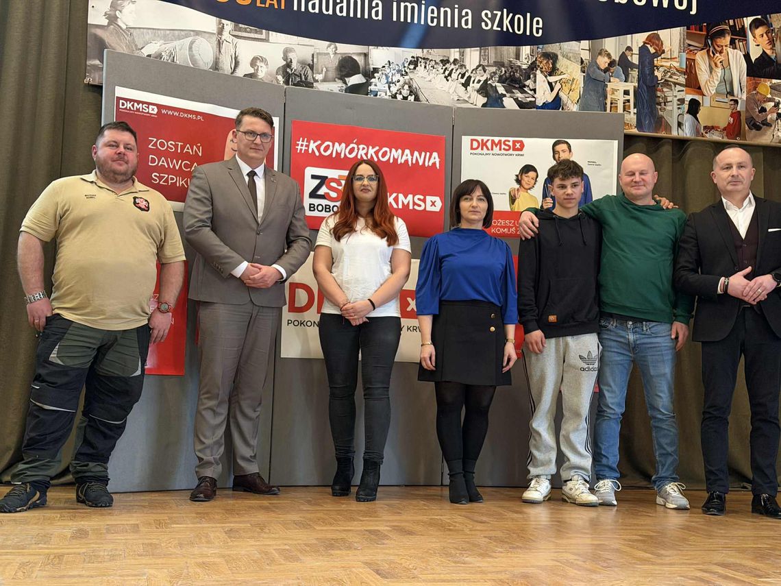 zdjęcie przedstawia grupę osób stojących przed ścianką reklamową