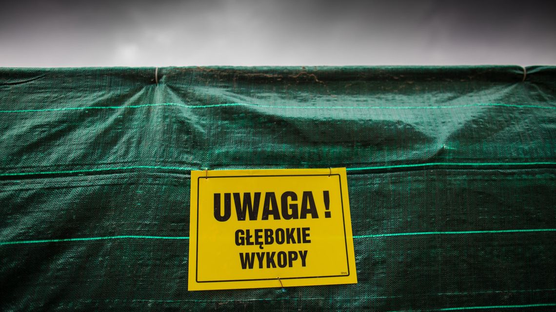 Ulica Graniczna w Gorlicach doczeka się remontu? Miasto rozmawia z Lasami Państwowymi żółta tabliczka z napisem uwaga, głębokie wykopy zawieszona na zielonym brezencie