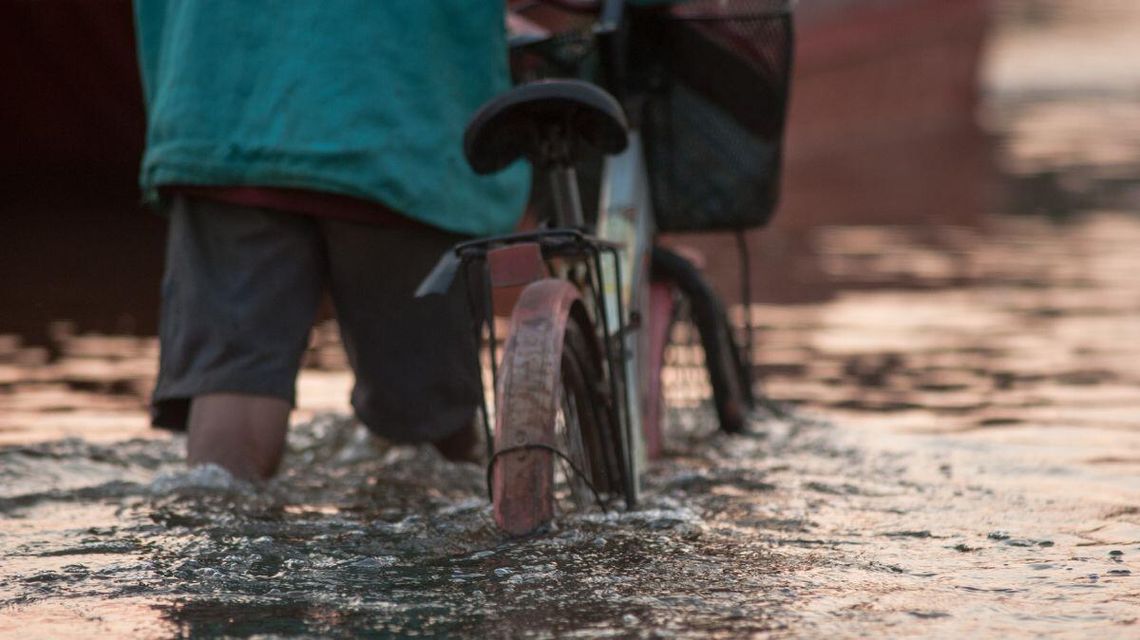 mężczyzna prowadzący rower przez drogę zalaną wodą