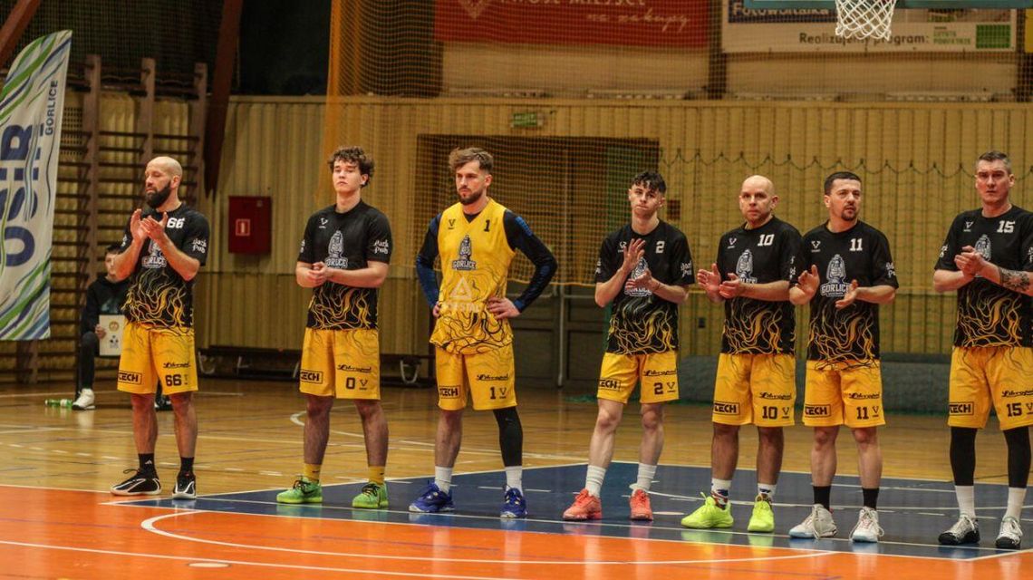 Walka o 2. ligę koszykówki trwa. Jakie wyniki półfinałów? zdjęcie przedstawia grupę sportowców w jednolitych koszulkach stojących na parkiecie pod koszem