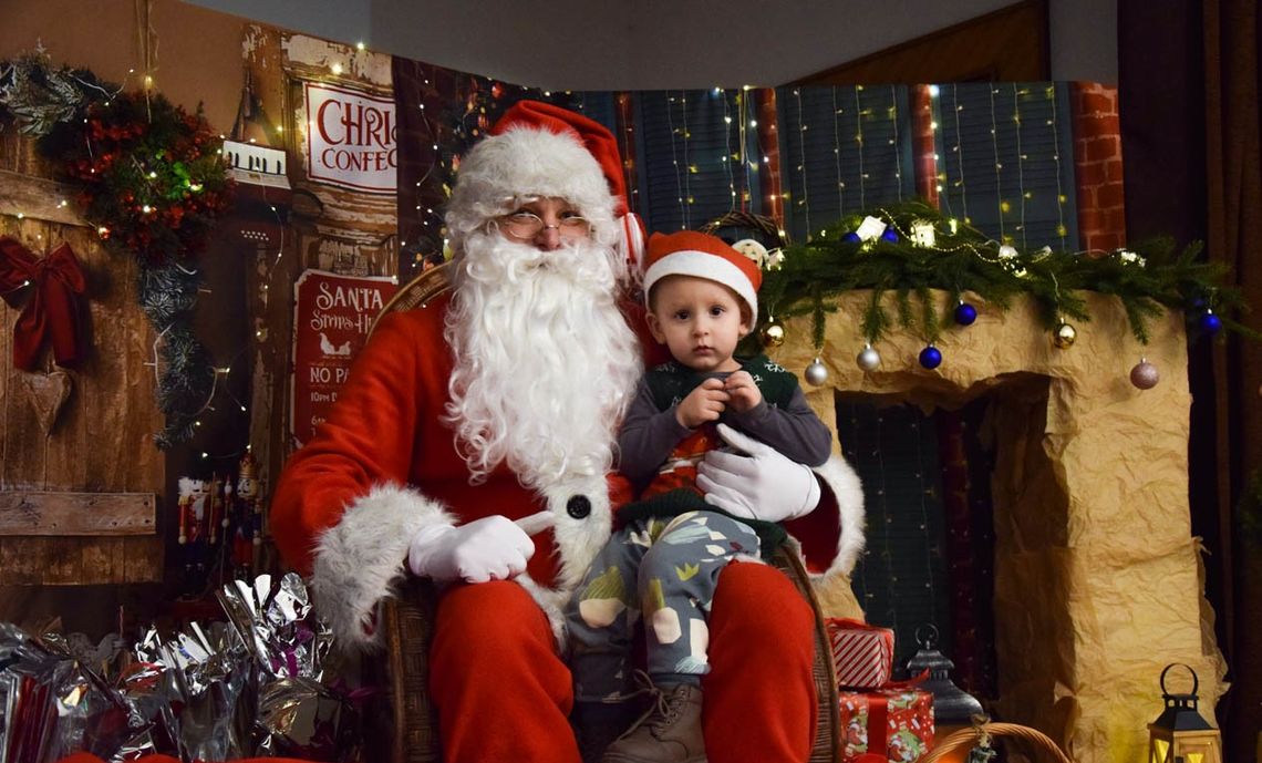 zdjęcie przedstawia Świętego Mikołaja trzymający dziecko z prezentem na kolanach