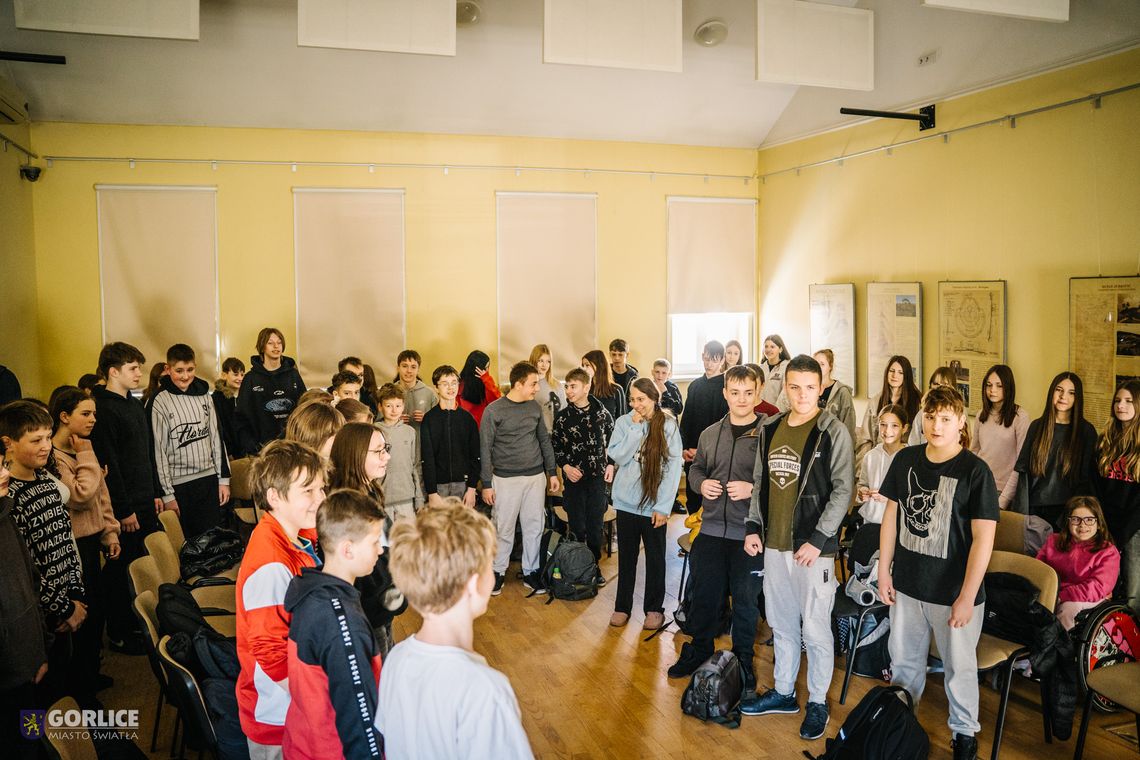 zdjęcie przedstawia stojących uczniów klas siódmych w klasie szkolnej