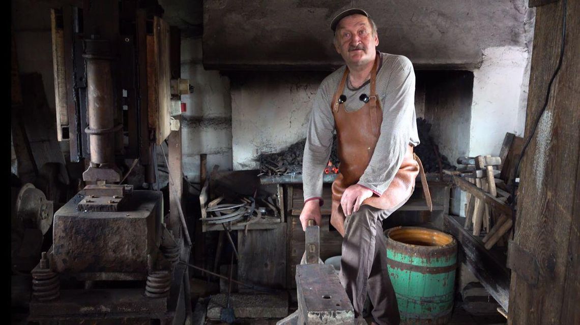 zdjęcie przedstawia mężczyznę z młotkiem i kowadłem w kuźni
