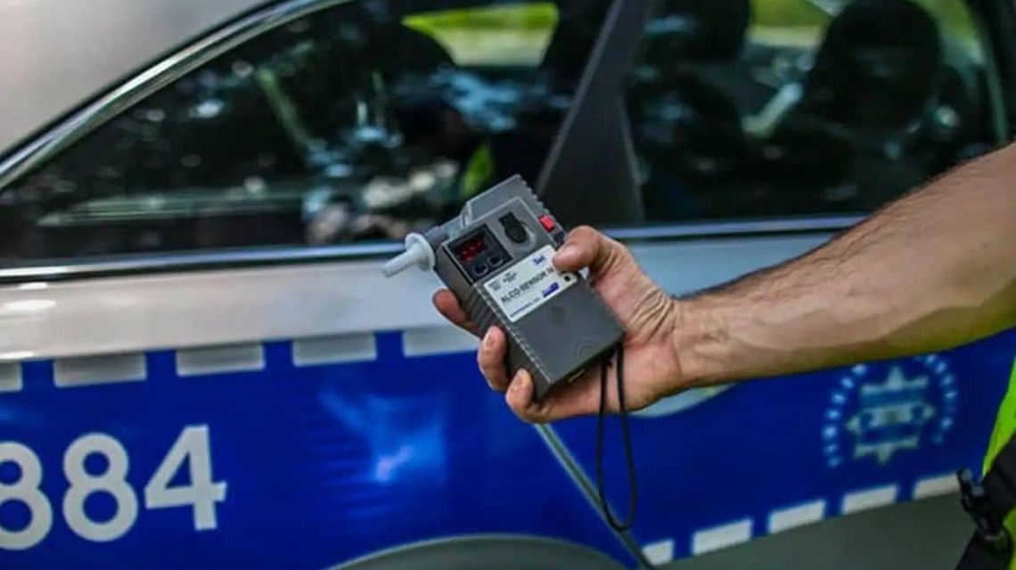 policjant trzymający w ręku alkomat w tle radiowóz policyjny