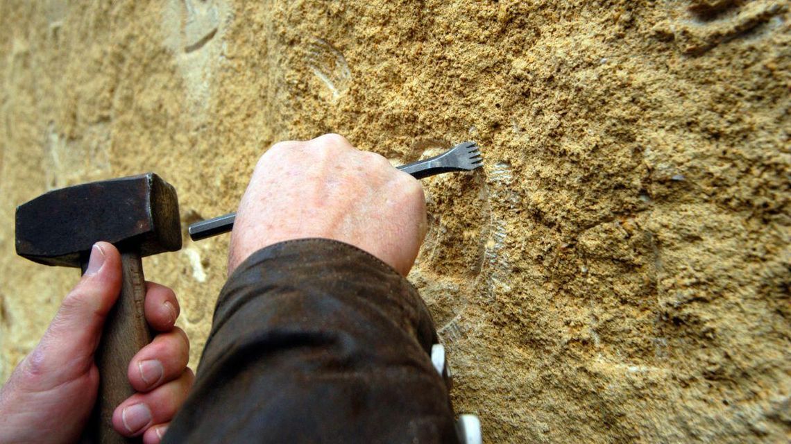 zdjęcie przedstawia pracownika, który dłutem ryje w kamieniu