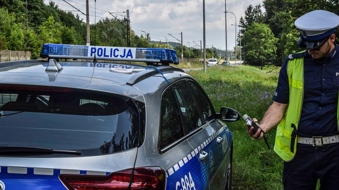 policjant stojący obok radiowozu trzymający alkomat