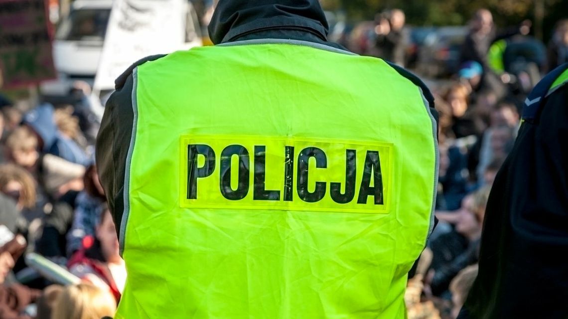 Policjant w żółtej kamizelce odblaskowej, widok na plecy z czarnym napisem policja