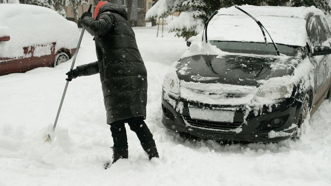 zdjęcie przedstawia kobietę odśnieżającą samochód