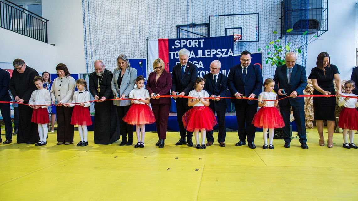 zdjęcie przedstawia grupę osób z czerwoną wstęgą