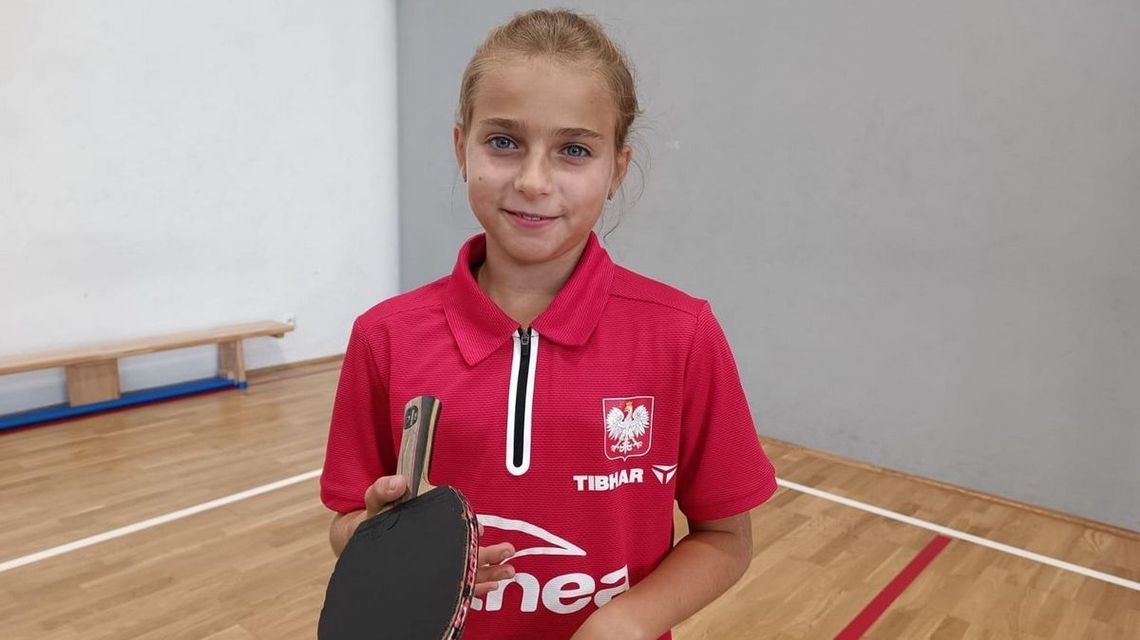 zdjęcie przedstawia dziewczynę w stroju sportowym z rakietką do ping-ponga w dłoni