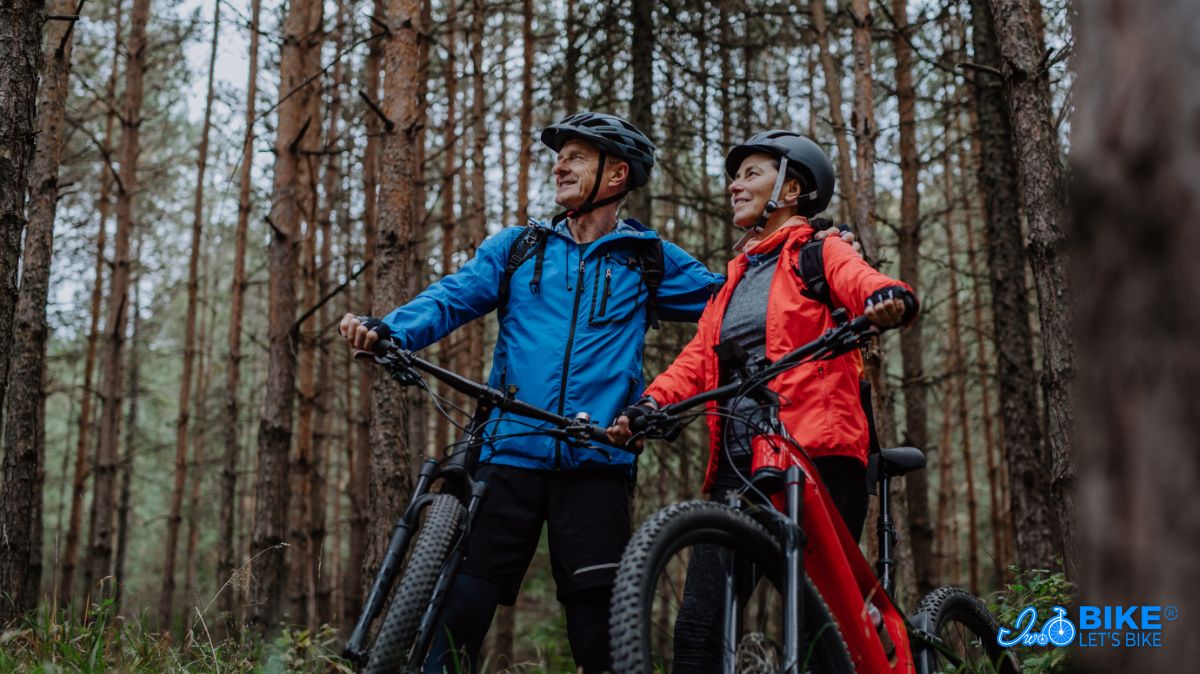 Starsze małżeństwo prowadzi swoje rowery elektryczne MTB na wycieczce w lesie, iwobike.pl